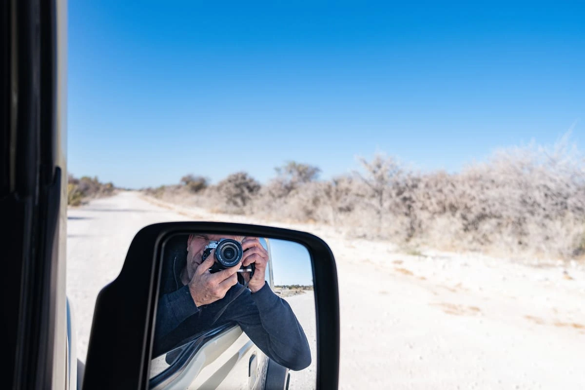 Frédéric prenant une photo du paysage aride et de la savane blanche du parc national d'Etosha à travers le rétroviseur latéral d'un 4x4