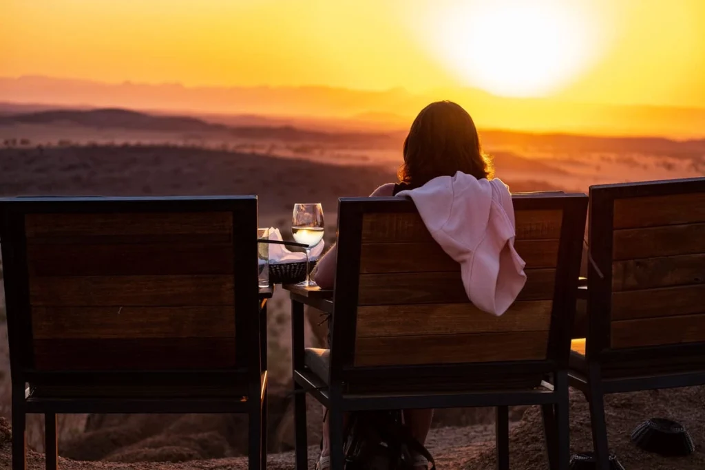 Femme de dos contemplant le coucher du soleil avec un verre de vin à Twyfelfontein en Namibie