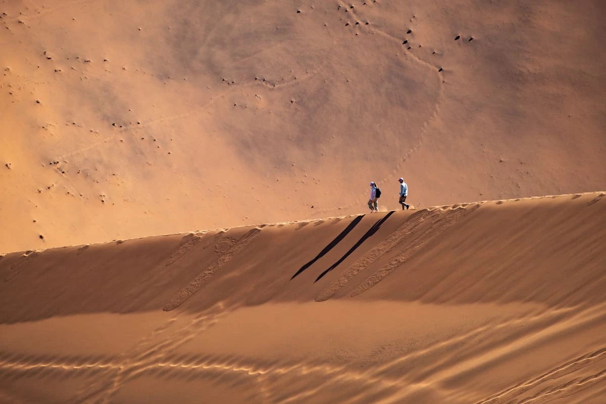Deux personnes marchant sur une dune de sable en Namibie avec leurs ombres