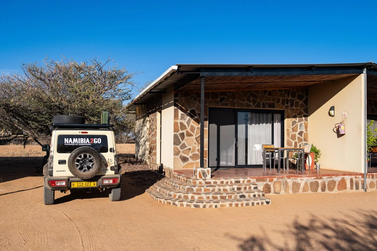 Un 4x4 stationné devant un bungalow en pierre au Ovita Wildlife Restcamp en Namibie
