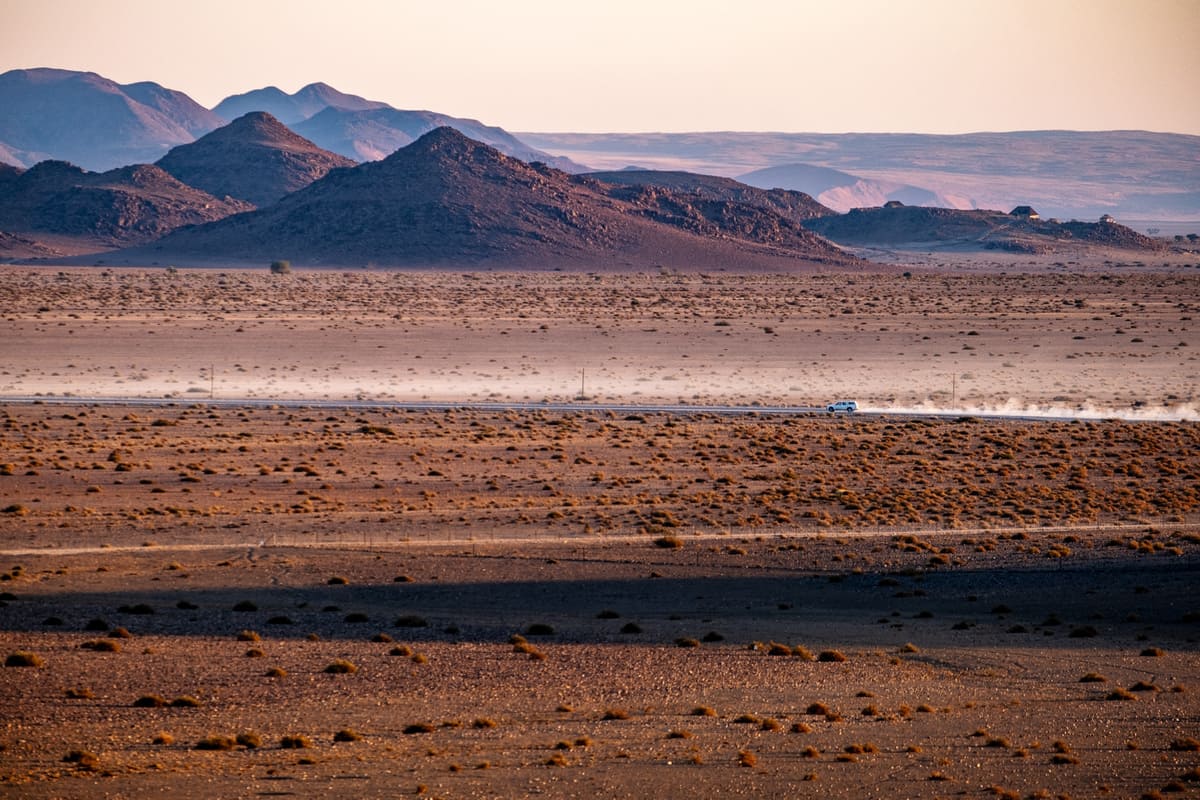 Traversée du désert du Namib en 4x4 : route poussiéreuse et montagnes arides sous une lumière de début de journée.