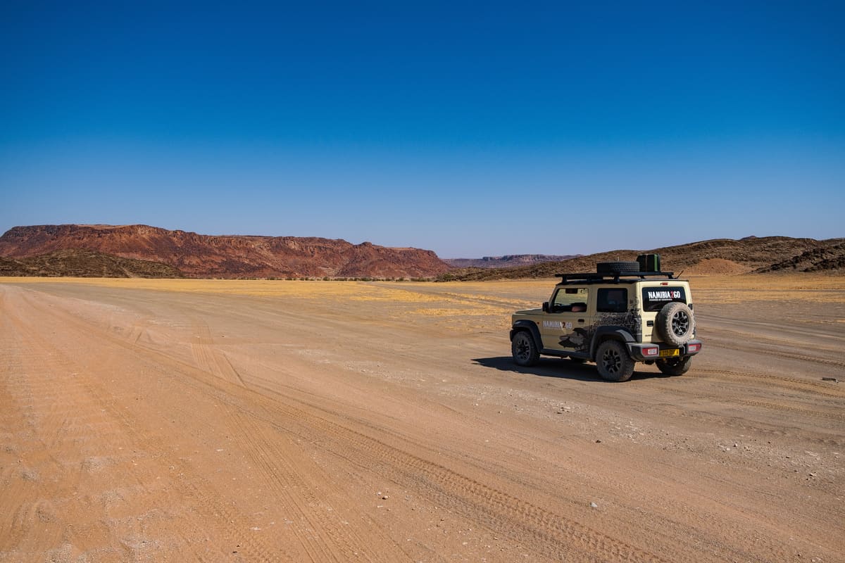 Road trip en 4x4 dans le Damaraland, Namibie, sur une route de gravier infinie sous un ciel bleu.