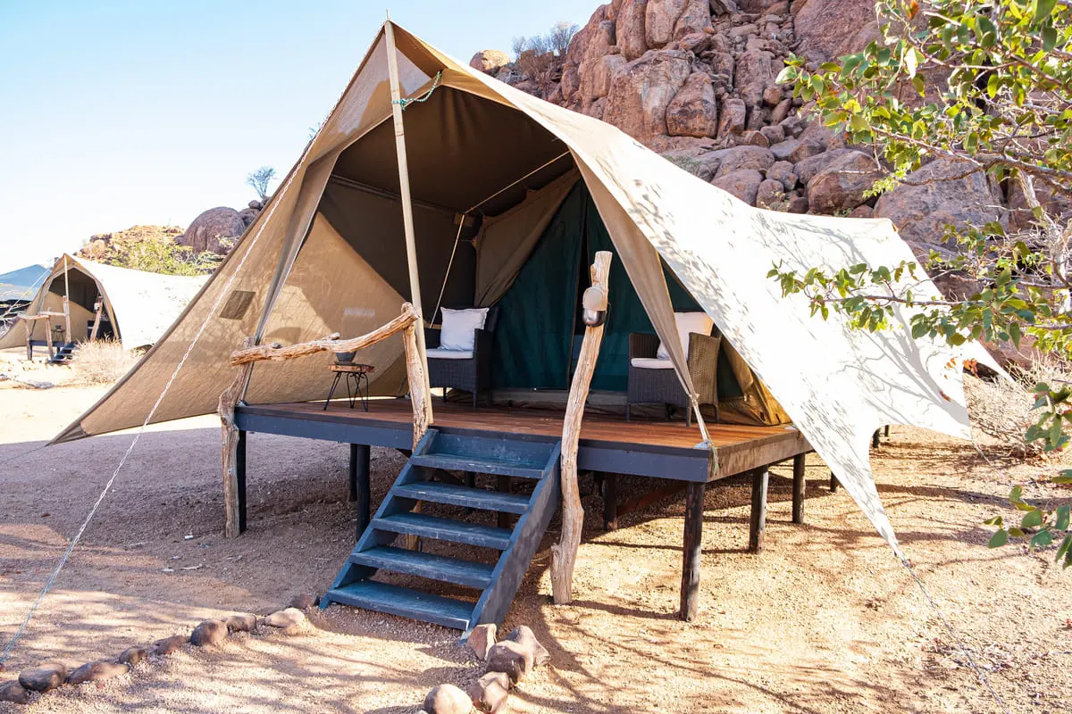 Tente de safari surélevée avec terrasse en bois au Twyfelfontein Adventure Camp, nichée au pied des rochers rouges du Damaraland.