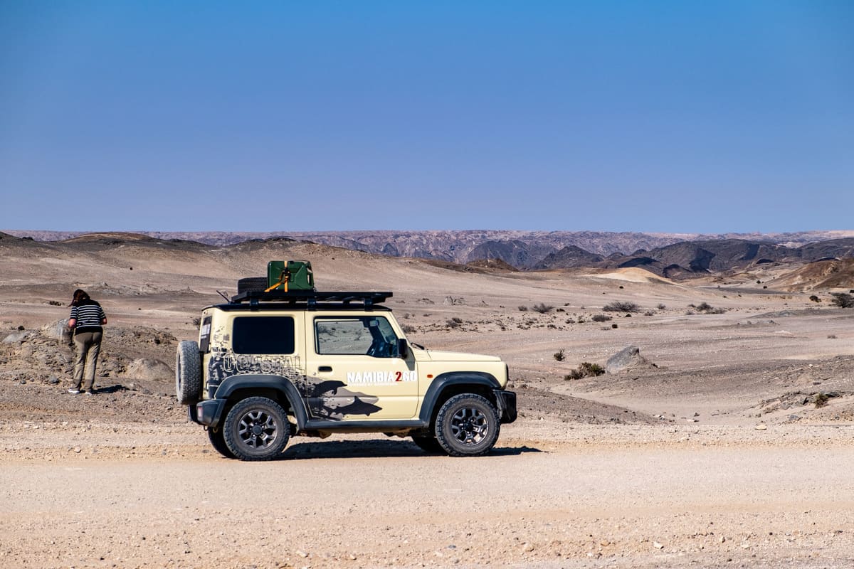 Un 4x4 Suzuki Jimny beige roulant sur une piste de gravier vers le Moon Landscape, un désert de collines érodées en Namibie.